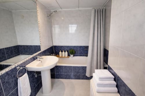 Baño moderno en Apartamento Salinas del hotel Aloha Calpe con lavamanos pedestal blanco, bañera con cortina de ducha y decoración oscura