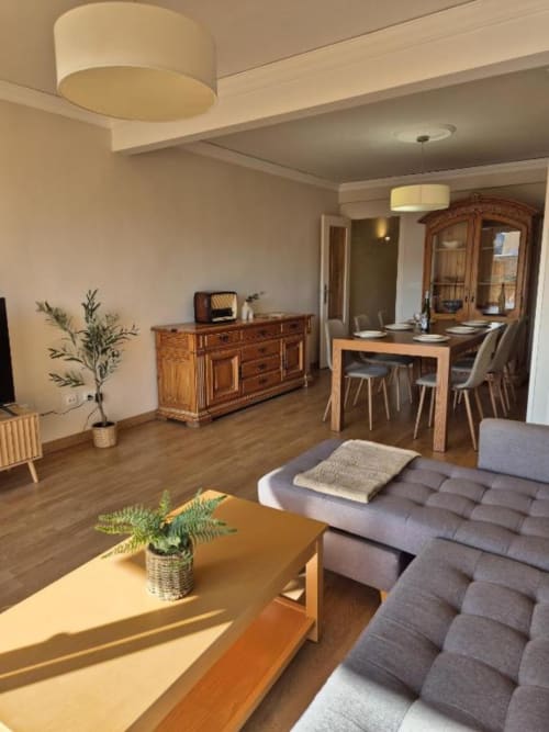 Luminosa sala de estar en apartamento antiguo de Calpe con muebles de madera, sofá gris, mesa de comedor y lámparas de techo modernas