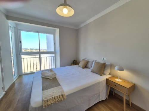 Dormitorio luminoso en apartamento de Calpe con balcón vista al mar, suelos de madera y mobiliario moderno