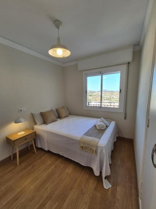 Dormitorio luminoso en apartamento del casco antiguo de Calpe con vistas al mar, balcón, suelos de madera, lámpara colgante y mobiliario moderno