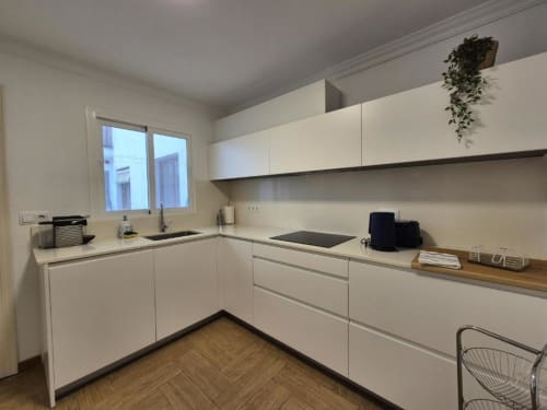 Cocina moderna blanca con electrodomésticos de acero inoxidable y suelos de parqué en el Apartamento Old Town Aloha Calpe, Calpe