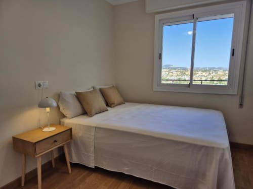 Dormitorio luminoso en apartamento Aloha Calpe con vistas al mar y montaña desde puertas correderas de cristal en Calpe, España.