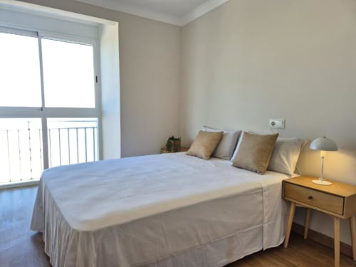 Luminoso dormitorio en apartamento del Casco Antiguo de Aloha Calpe con balcón con vistas al mar, mesilla de madera y comodidades modernas