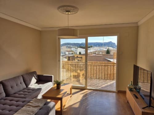 Salón moderno en apartamento de Calpe con sofá gris, mesa de madera y amplias puertas hacia terraza con vistas a montaña y mar