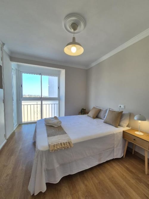 Dormitorio luminoso en Apartamento Aloha Calpe Old Town con vistas al mar, lámpara colgante moderna, suelos de madera y acceso a balcón