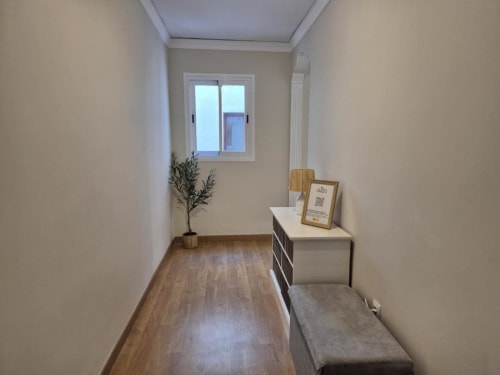 Luminoso pasillo en apartamento del casco antiguo de Aloha Calpe con suelos de madera, ventana, planta y banco de almacenamiento