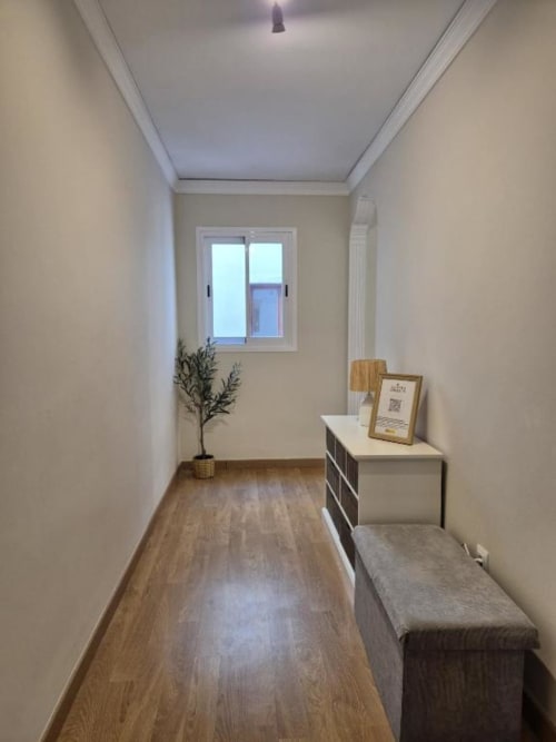 Luminoso pasillo moderno en apartamento del Casco Antiguo de Aloha Calpe con suelos de madera, ventana, planta y banco de almacenamiento