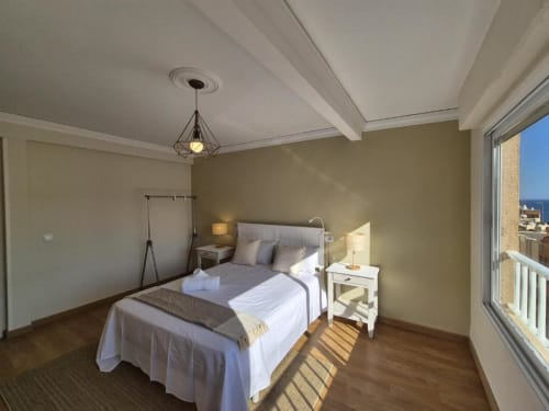 Dormitorio luminoso en Apartamento Old Town Aloha Calpe con vistas al mar, cama de metal, ropa de cama blanca, suelos de madera y balcón
