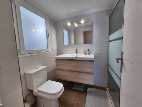 Baño moderno en Aloha Calpe Old Town Apartment, Calpe, con tocador de madera, inodoro blanco, espejo iluminado y ventana.