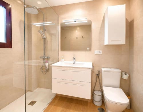 Baño moderno en Dreams Apartment de Aloha Calpe con ducha a ras de suelo, tocador blanco, inodoro y toallero calefactable