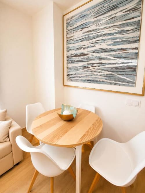 Área de comedor moderno en Dreams Apartment de Aloha Calpe con mesa redonda de madera, sillas blancas y cuadros abstractos enmarcados.