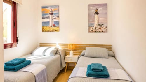 Dos camas individuales con toallas color turquesa en Dreams Apartment de Aloha Calpe, Calpe, con cuadro de faro encima