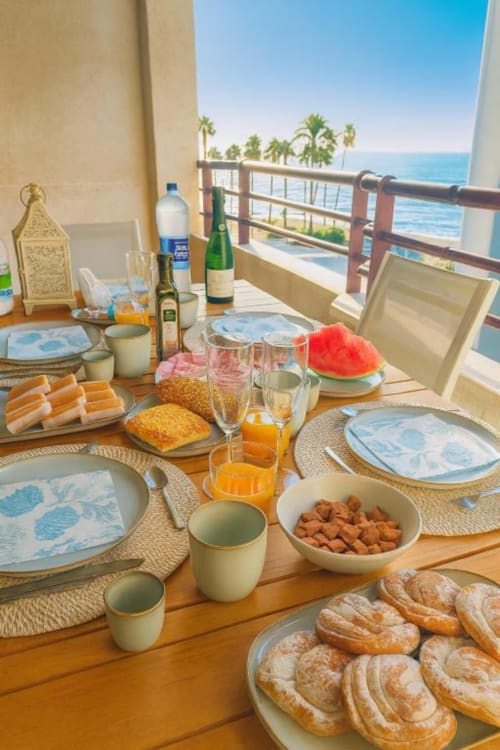 Desayuno frente al mar en Aloha Calpe con vistas al océano, pasteles, frutas frescas y vino en la mesa