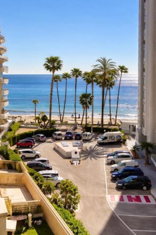 Vista del balcón del apartamento Aloha Calpe Dreams con playa mediterránea, palmeras y zona de aparcamiento