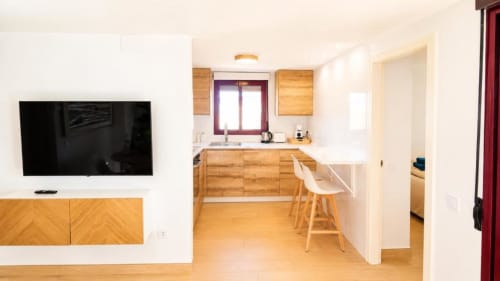 Moderna cocina y sala de estar en Dreams Apartment del hotel Aloha Calpe con muebles de madera, barra desayunadora y pantalla plana