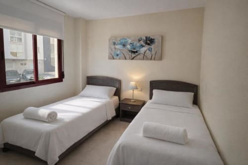 Dormitorio doble en Aloha Calpe Sea Palm Apartment, Calpe con ropa de cama blanca, marcos de madera oscura y obra de arte floral azul
