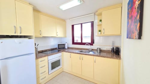 Cocina amarillo brillante con electrodomésticos color crema, encimeras de granito y vistas al mar en Aloha Calpe Sea Palm Apartment en Calpe