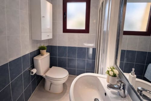 Baño moderno en el apartamento Aloha Calpe Sea Palm, Calpe, con azulejos azul oscuro y claros, inodoro, lavabo, bañera y ventana