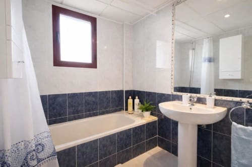 Baño moderno del apartamento Sea Palm de Aloha Calpe en Calpe con azulejos oscuros, bañera, lavamanos de pedestal y ventana