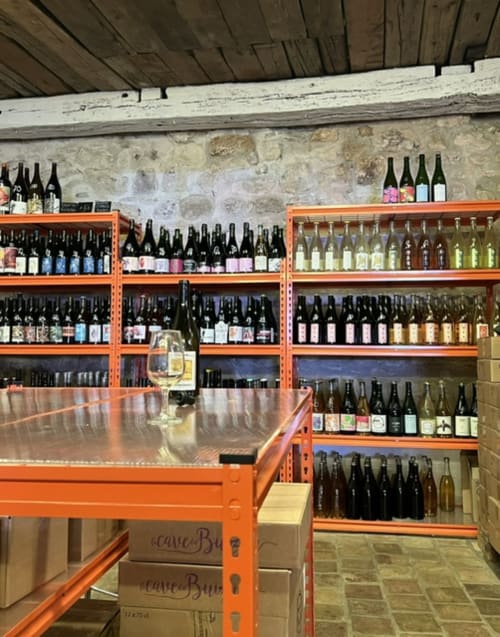 Salle de dégustation à La Maison d'Ambronay avec rayonnages orange présentant des bouteilles et un verre de vin sur le comptoir