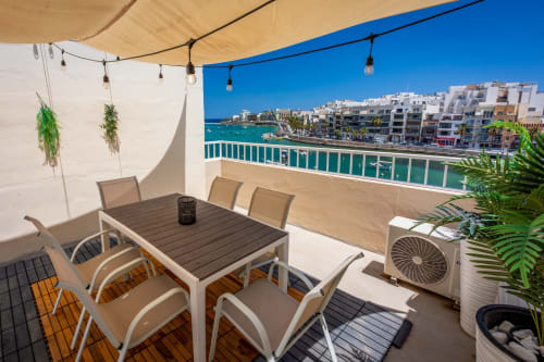 Terrazza vista mare presso Calm Holiday Homes a Marsa con tavolo da pranzo, vedute sul mare e edifici costieri mediterranei.