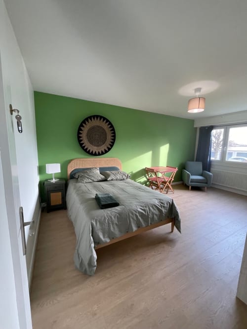 Spacious green bedroom at Mattbnb Metz with wooden bed, desk, chair, and city views through windows