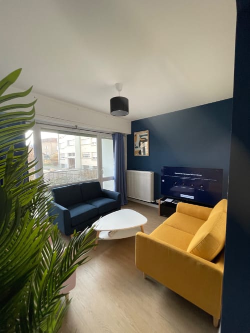 Séjour moderne chez Mattbnb Metz avec fauteuil jaune, canapé bleu, table blanche et espace divertissement TV