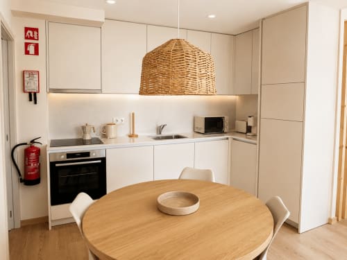 Cozinha moderna no Terra Clara Studio em Esposende com armários brancos, luminária pendente tecida e mesa de jantar em madeira