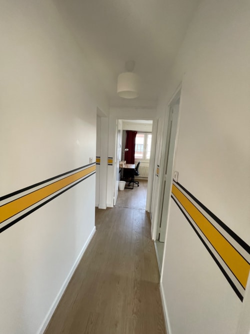 Couloir moderne avec rayures jaunes et noires à Mattbnb Metz, menant à une chambre d'hôte dotée d'un bureau et d'une vue sur fenêtre