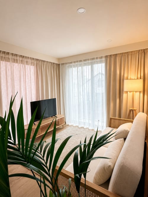 Aconchegante sala de estar moderna com sofá creme, TV de tela plana, plantas em vasos e cortinas do piso ao teto no Terra