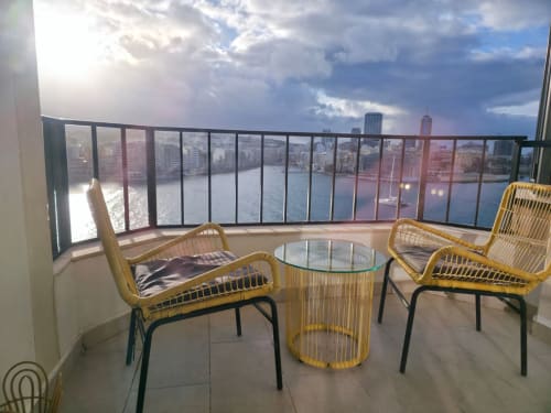 Moderna zona relax su balcone con sedie gialle intrecciate affacciata sul lungomare di Sliema e lo skyline di San Julians, Malta