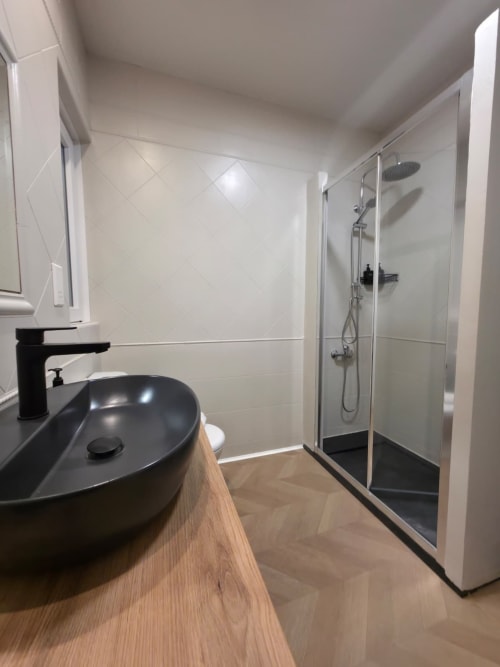 Bagno moderno nell'appartamento Calm Holiday Homes, San Julian's, con lavabo nero, doccia walk-in, piastrelle bianche e pavimento in legno