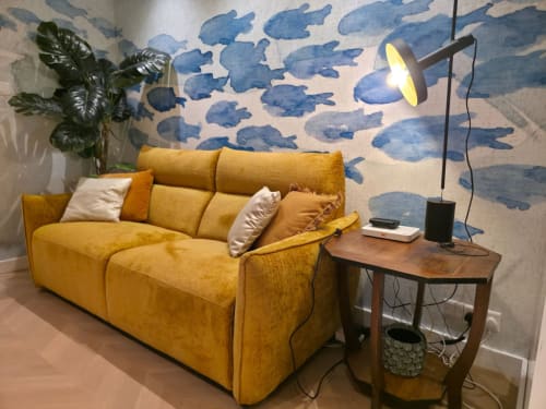Divano giallo moderno con cuscini in luminoso soggiorno, carta da parati azzurra a nuvole, tavolino in legno, pianta in vaso