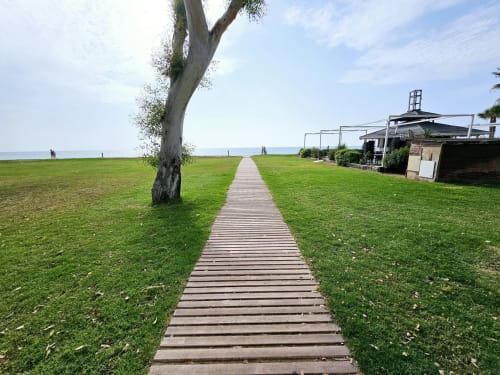 Pasarela de madera entre frondosos jardines de la casa de playa Monica Socarici en Benicàssim con vistas al mar