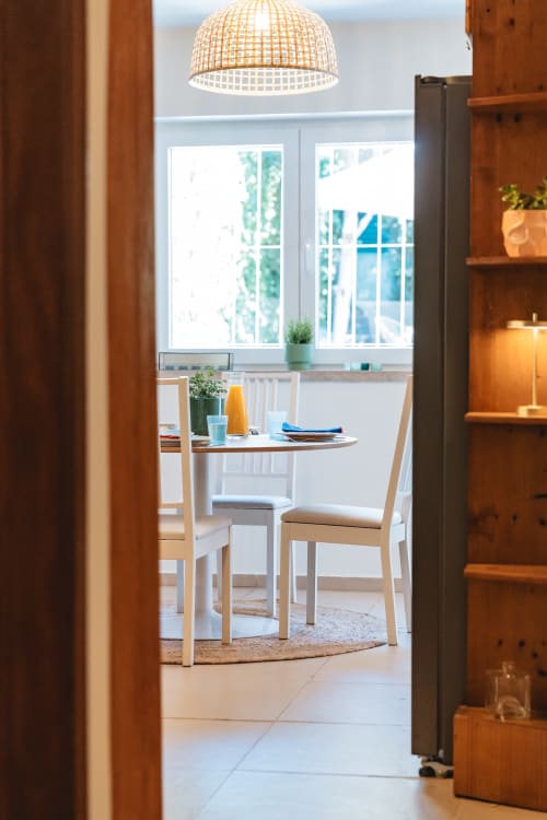 Bright dining area in Cascais Garden House with round table, wooden chairs, pendant lamp, and garden views through windows