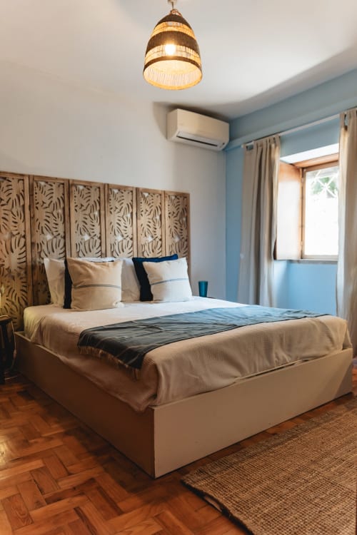 Modern bedroom at Arestas e Planetas in Cascais with decorative headboard, cream bedding, pendant light, and garden views
