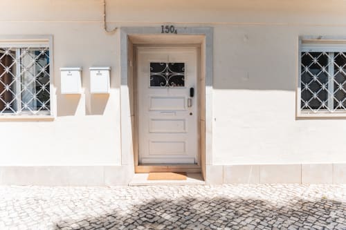 Cascais Garden House entrance at 150A with pale wooden door, decorative windows, and cobblestone courtyard in Portugal