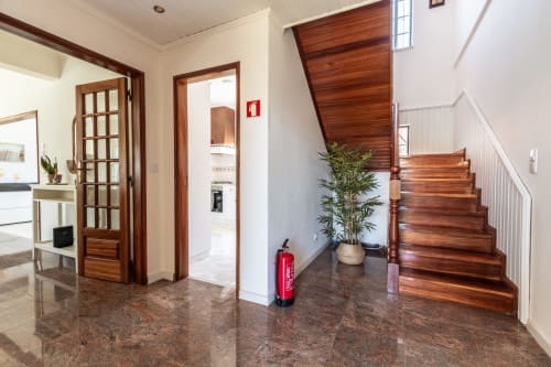 Entrada moderna de villa em Amora com escadas em madeira, piso polido, planta em vaso e extintor de incêndio vermelho
