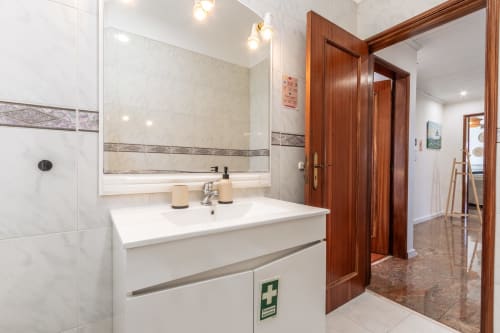 Banheiro moderno com bancada branca, espelho grande, azulejos de mármore e portas de madeira na villa Arestas e Planetas em Amora