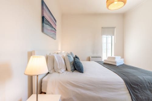 Quarto luminoso da vila Arestas e Planetas perto de Caparica com cama branca, almofadas decorativas, luminária lateral e vista para o jardim
