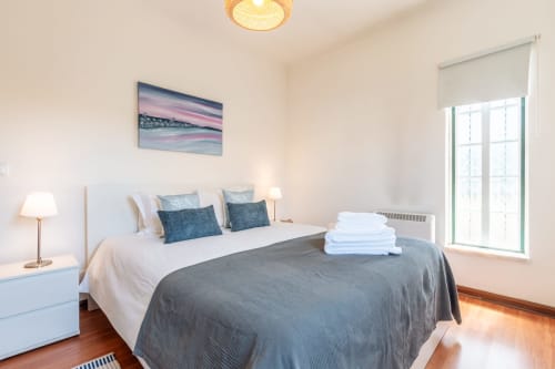 Quarto luminoso na villa Arestas e Planetas em Amora com cama queen, tons azuis, arte costeira e vista para o jardim
