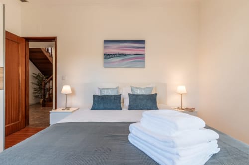 Quarto moderno com roupa de cama branca, almofadas azuis, arte de praia e abajures na villa Arestas e Planetas em Amora, Portugal