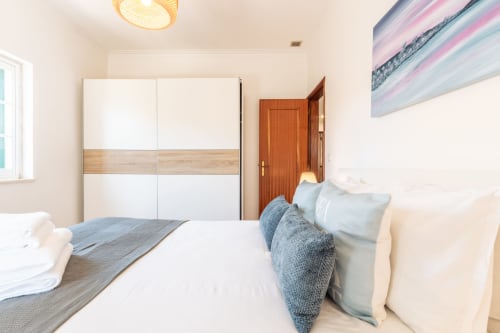 Quarto luminoso na villa Arestas e Planetas em Amora com cama branca, guarda-roupa moderno deslizante e porta de madeira