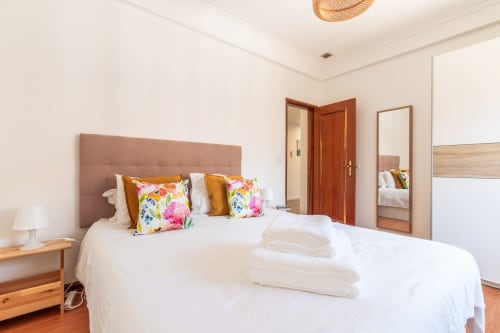 Quarto luminoso com cabeceira rosa, almofadas floridas e mesa-de-cabeceira de madeira na villa Arestas e Planetas em Amora, Portugal
