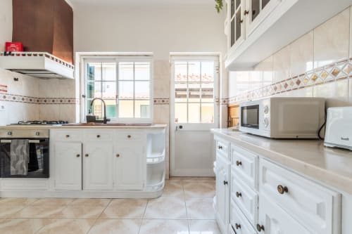 Cozinha moderna branca com bancadas de azulejos, fogão, micro-ondas e vista para o jardim na villa Amora