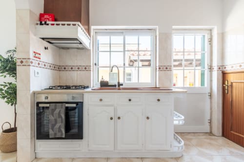 Cozinha moderna branca com fogão a gás, forno, máquina de lavar louça e amplas janelas com vista para o jardim da villa Amora