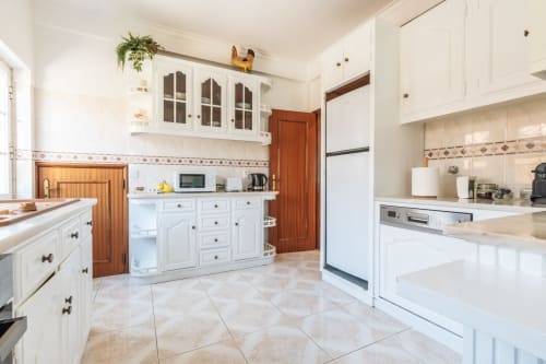 Cozinha moderna branca com acabamentos em madeira, eletrodomésticos em aço inoxidável e piso em azulejo terracota na villa Amora perto de