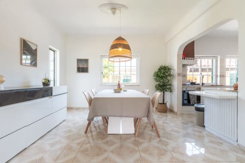 Sala de jantar moderna na villa Amora com mesa redonda, luminária de fibra trançada e cozinha aberta com vista para o jardim