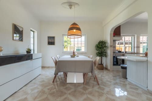 Área de jantar moderna na villa Amora com iluminação pendente, mesa branca, cadeiras bege e cozinha aberta