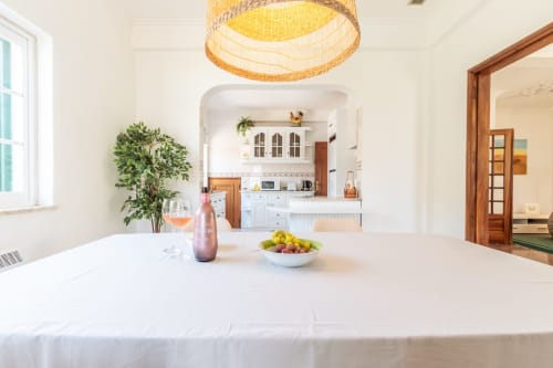 Cozinha e sala de jantar modernas na villa Amora com marcenaria branca, luminária de fibra natural e vista para o jardim